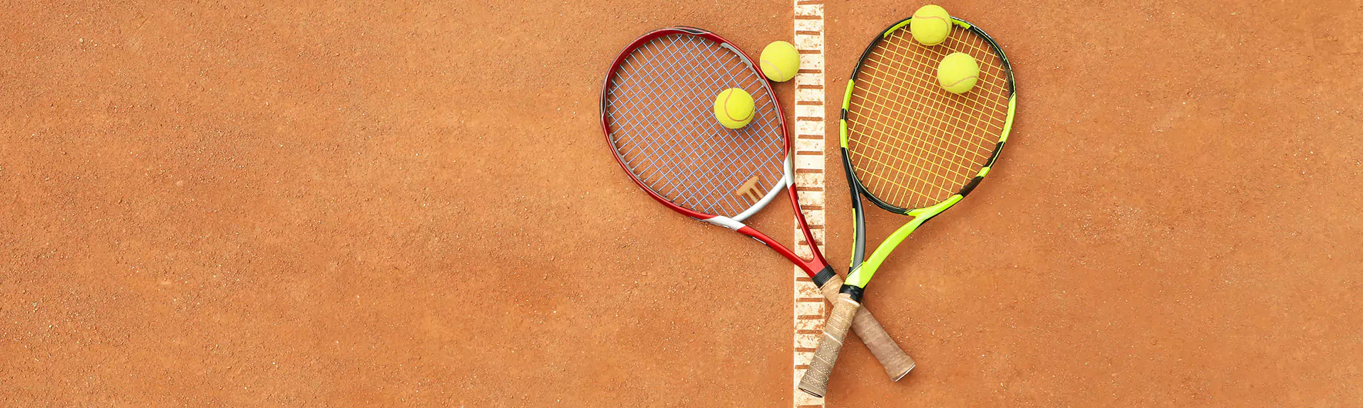 2 Tennisschläger mit Tennisbällen, die auf einem Sandplatz liegen