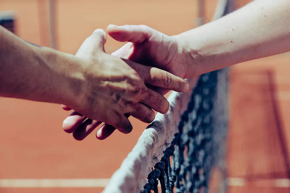 handshake 2 Personen reichen sich an einem Tennisnetz nach dem Match die Hand