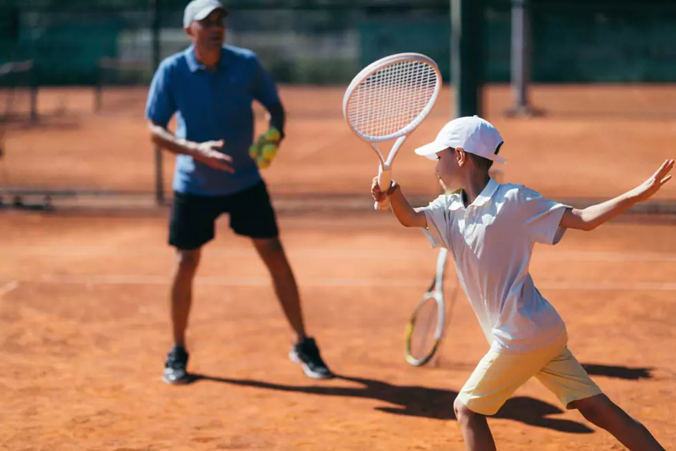 Tennistrainer gibt jungem Spieler Anweisungen während des Trainings