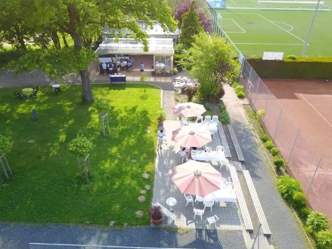 Blick auf das Klubhaus mit Tischen, Stühlen und Schirmen im Außenbereich