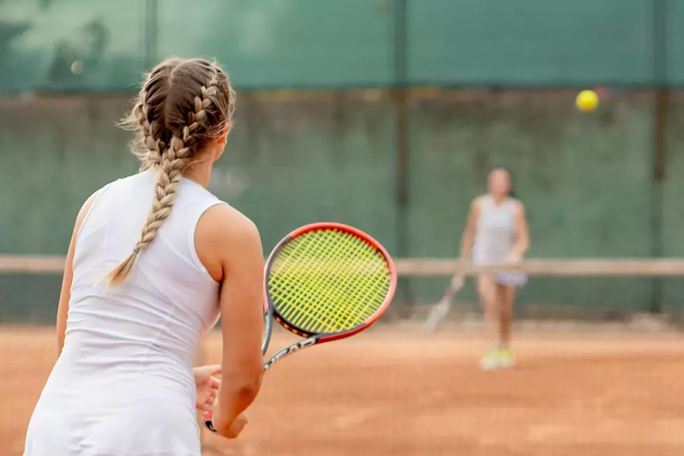 2 junge Frauen spielen Tennis auf einem Sandplatz.