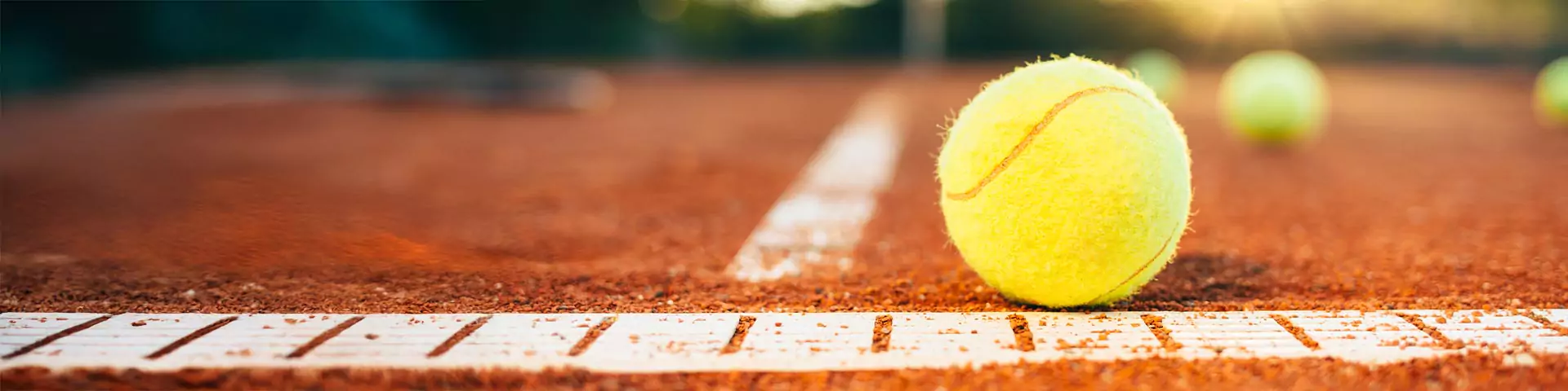 Tennisball Nahaufnahme eines Tennisballs auf einem Sandplatz auf der weißen Linie. 2 weitere Tennisbälle unscharf im Hintergrund.