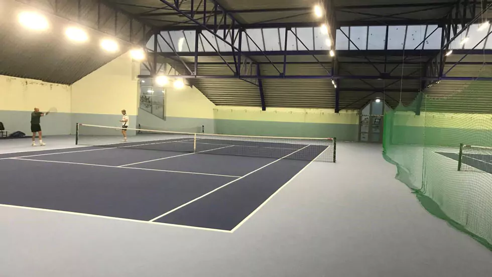 Blick in eine Tennishalle mit 2 Plätzen und 2 Personen beim Tennistraining.