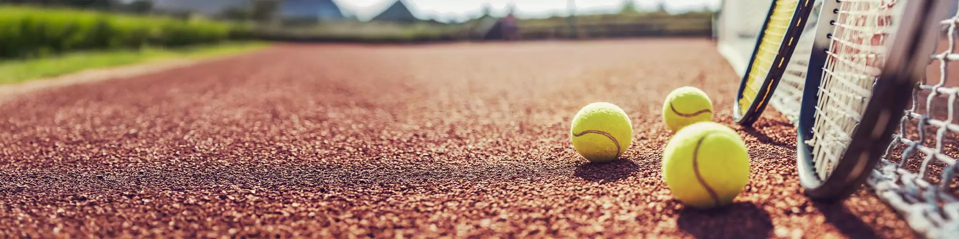 Tennisschläger am Netz 2 Tennisschläger lehnen an einem Tennisnetz auf einem Sandplatz. 3 Tennisbälle im Vordergrund.